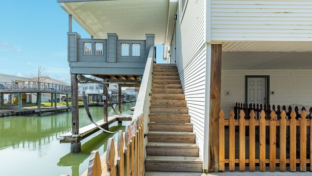 A waterfront property with a wooden staircase leading to a covered deck, a wooden fence, and a view of the water. - Spacious 4-bedroom house in lovely Jamaica Beach with AC (Jamaica Beach)
