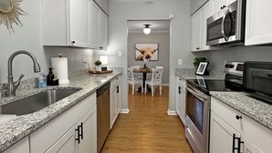 Una cocina moderna con encimeras de granito, electrodomésticos de acero inoxidable y armarios blancos.