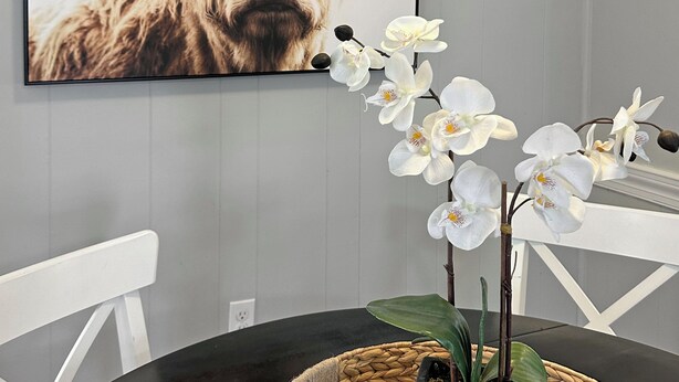 Un comedor con una mesa redonda, una cesta tejida con una planta en maceta y una obra de arte enmarcada de un rostro de vaca en la pared.
