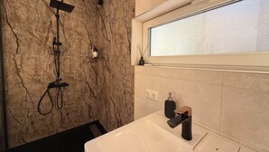 A modern bathroom with a marble wall, a built-in shower, a window, and a white bathtub. - Lakefront Cabin w/ Sauna & Hot Tub | Aiyana Retreat (Gauja)