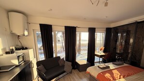 A modern hotel room with a bed, a sofa, a small table, a desk, and a kitchenette. - Lakefront Cabin w/ Sauna & Hot Tub | Aiyana Retreat (Gauja)