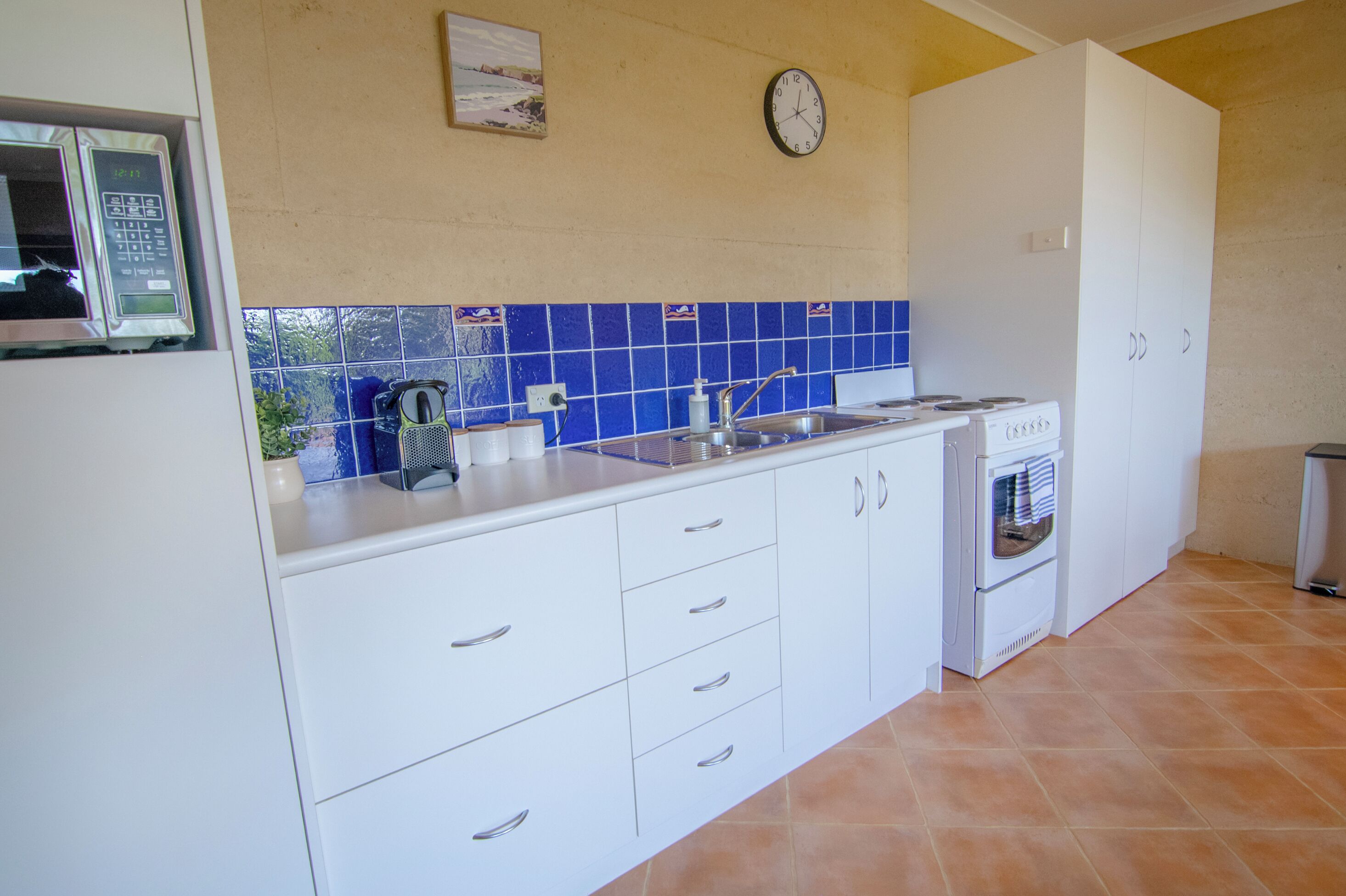 A kitchen with white cabinets, a blue tiled backsplash, a clock, and a stove.