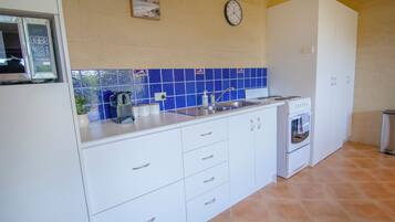 A kitchen with white cabinets, a blue tiled backsplash, a clock, and a stove.