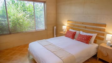 A bedroom with a large bed, wooden headboard, two bedside tables with lamps, and a window with blinds.