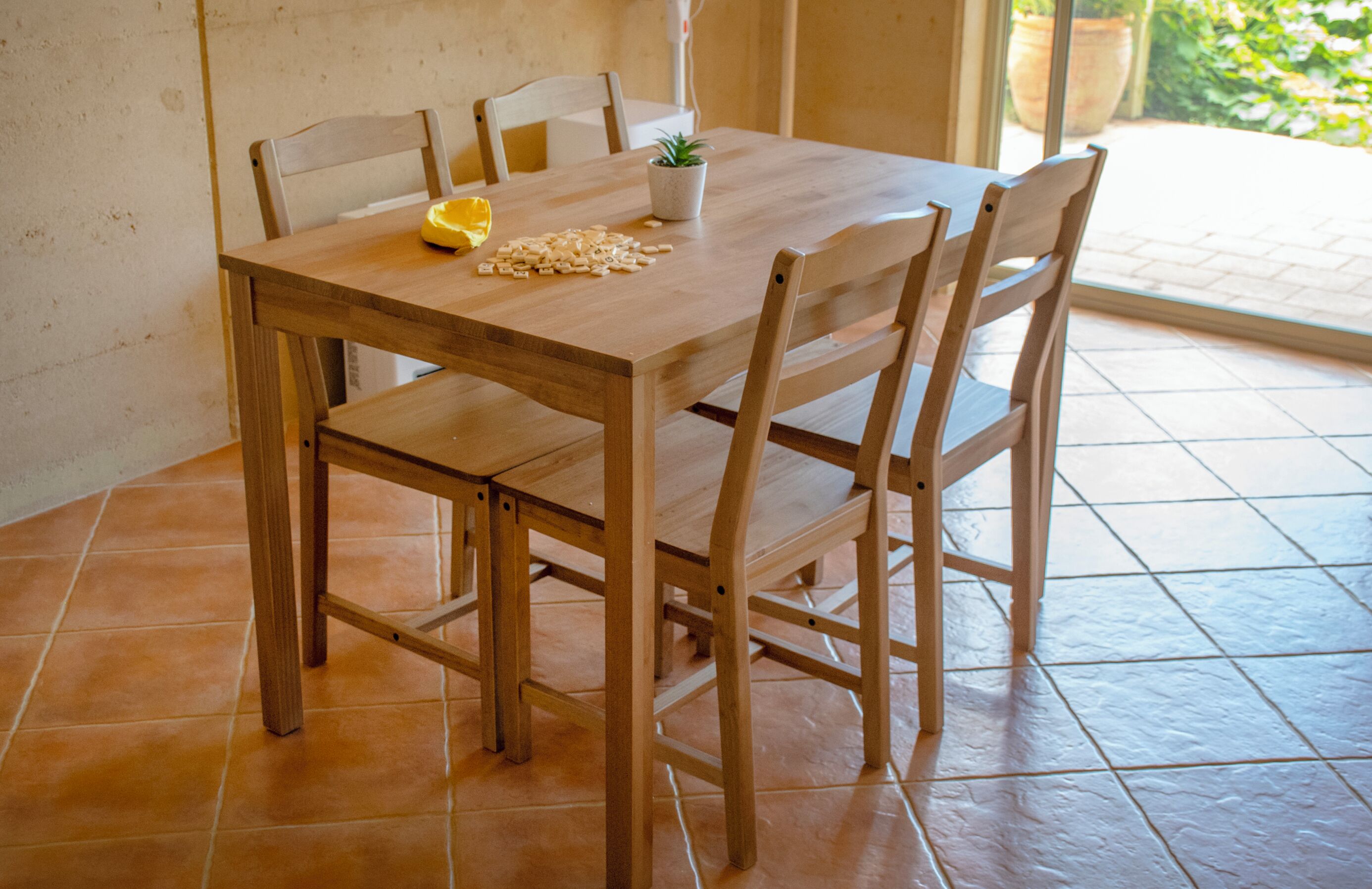 A wooden dining table with four chairs, a potted plant, and a yellow object on the table.
