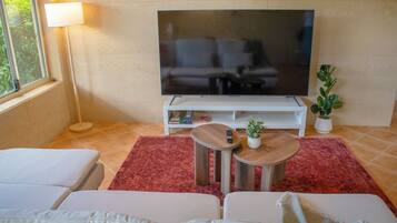 A living room with a flat-screen TV, a sofa, a coffee table, a lamp, and a potted plant.