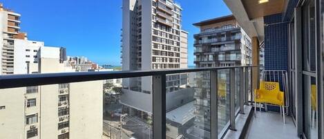 A balcony with a view of city buildings, a yellow chair, and a glass railing.