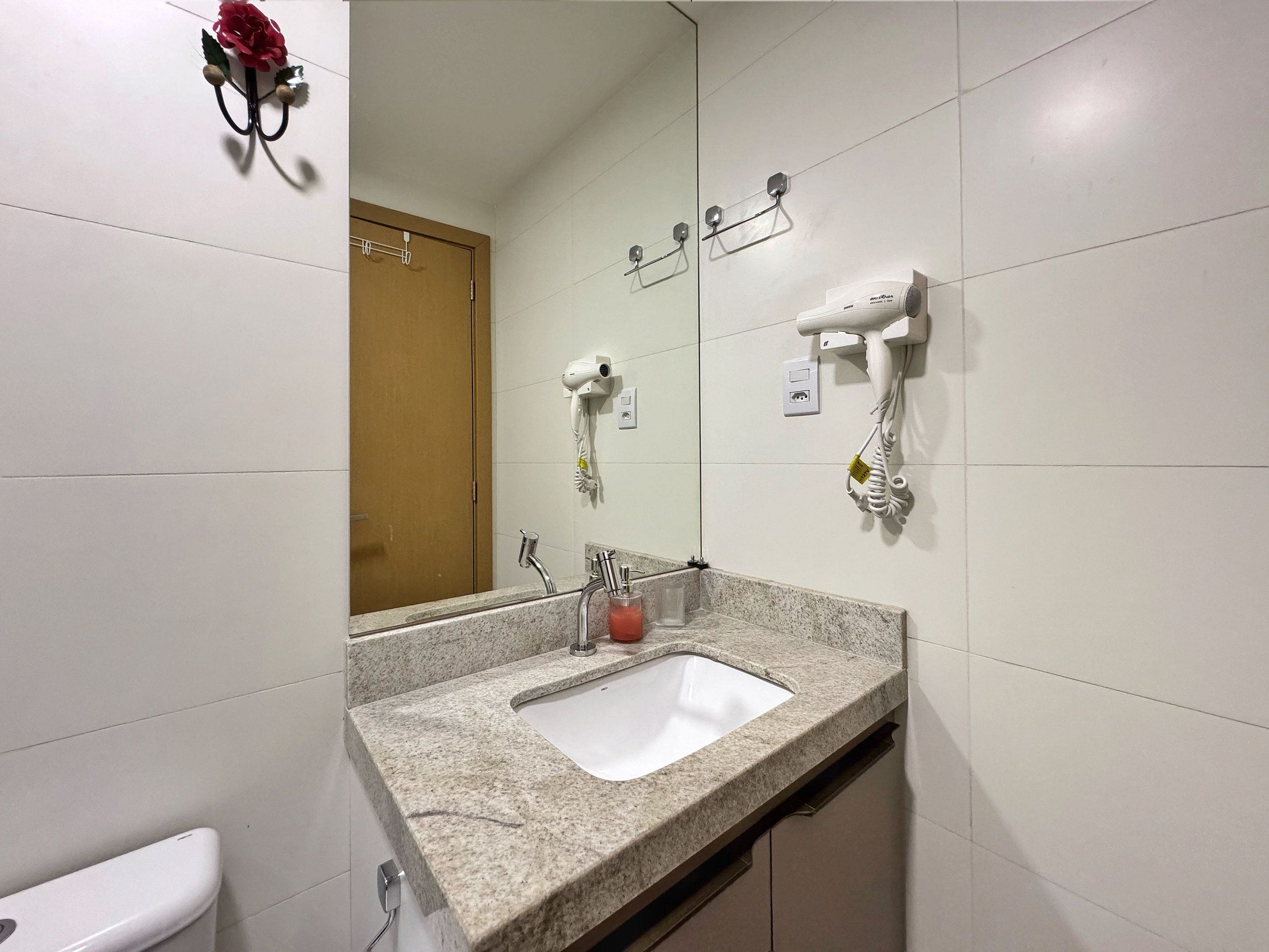 Un bagno con lavandino, specchio, porta asciugamani e asciugacapelli fissato alla parete.