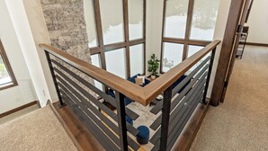 A modern interior with a wooden staircase, large windows, and a stone accent wall. - Plum Creek Lodge • Expansive Mountain Views • 6BR • 5.5BA • Game Room (Cle Elum)