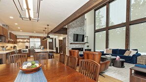 A spacious kitchen with modern appliances, a dining area with a wooden table and chairs, and a cozy living room with a blue sofa and fireplace. - Plum Creek Lodge • Expansive Mountain Views • 6BR • 5.5BA • Game Room (Cle Elum)
