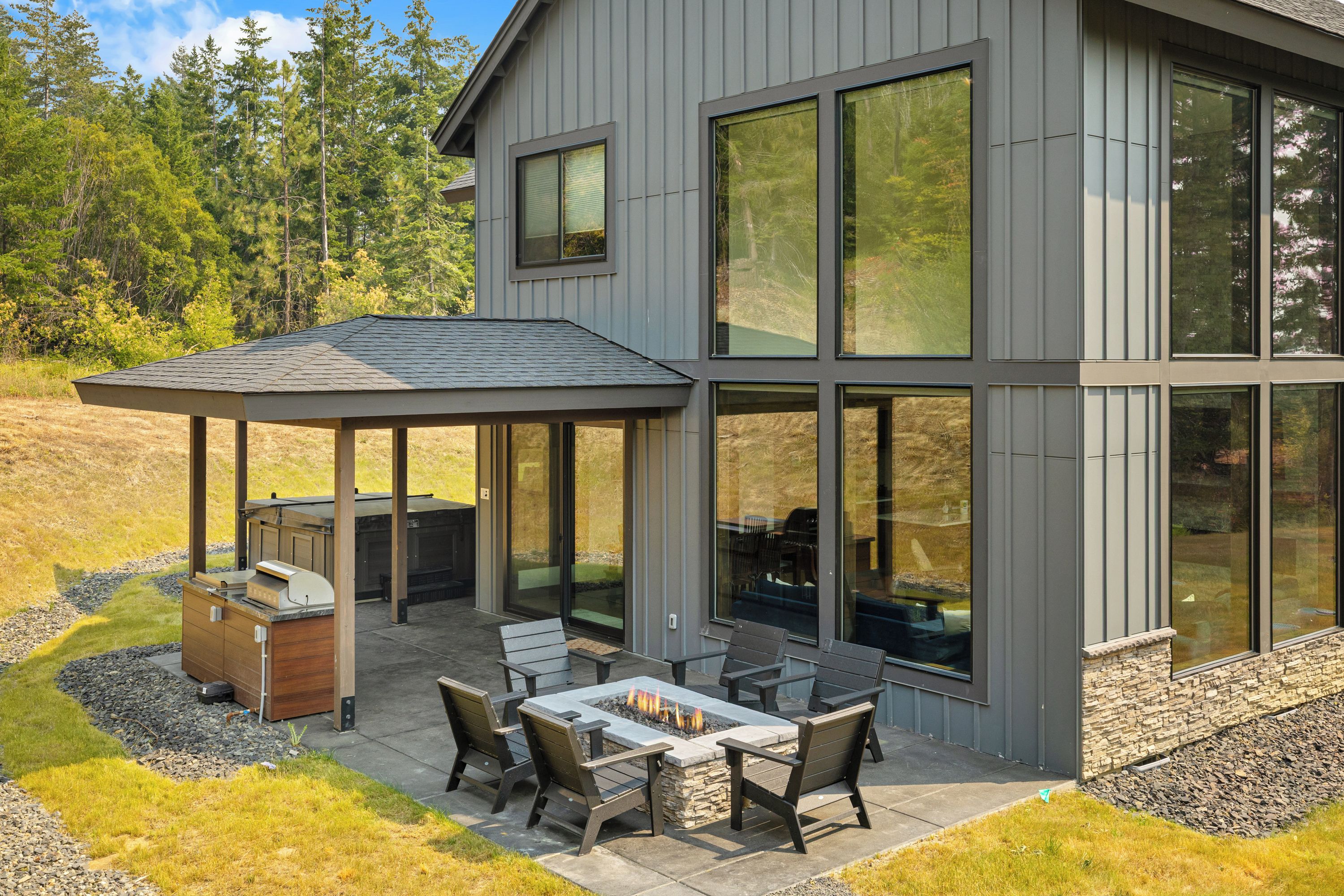 A modern house with a covered patio, outdoor seating, and a fire pit.