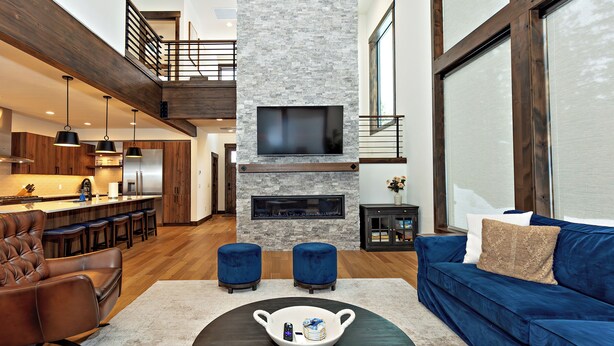 A modern living room with a fireplace, a blue sofa, and a dining area with wooden furniture. - Plum Creek Lodge • Expansive Mountain Views • 6BR • 5.5BA • Game Room (Cle Elum)