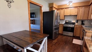 A kitchen with wooden cabinets, a black refrigerator, a stove, and a dining table with a white frame. - Mountain-View 3BR Home w/ Firepit • Hatfield AR (Hatfield)