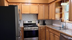 A kitchen with wooden cabinets, a black refrigerator, stainless steel appliances, and a window. - Mountain-View 3BR Home w/ Firepit • Hatfield AR (Hatfield)