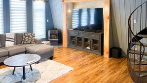 A cozy living room with a wooden floor, a sofa, a coffee table, a fireplace, and a TV. - Grand Marais Retreat *Hot tub* (Grand Marais)