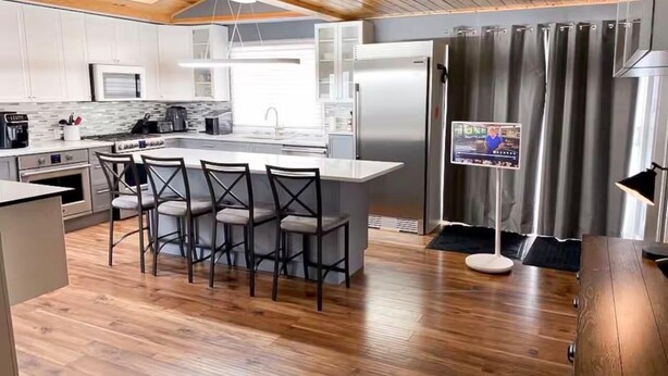 A modern kitchen with a central island, bar stools, a refrigerator, and a television. - Grand Marais Retreat *Hot tub* (Grand Marais)
