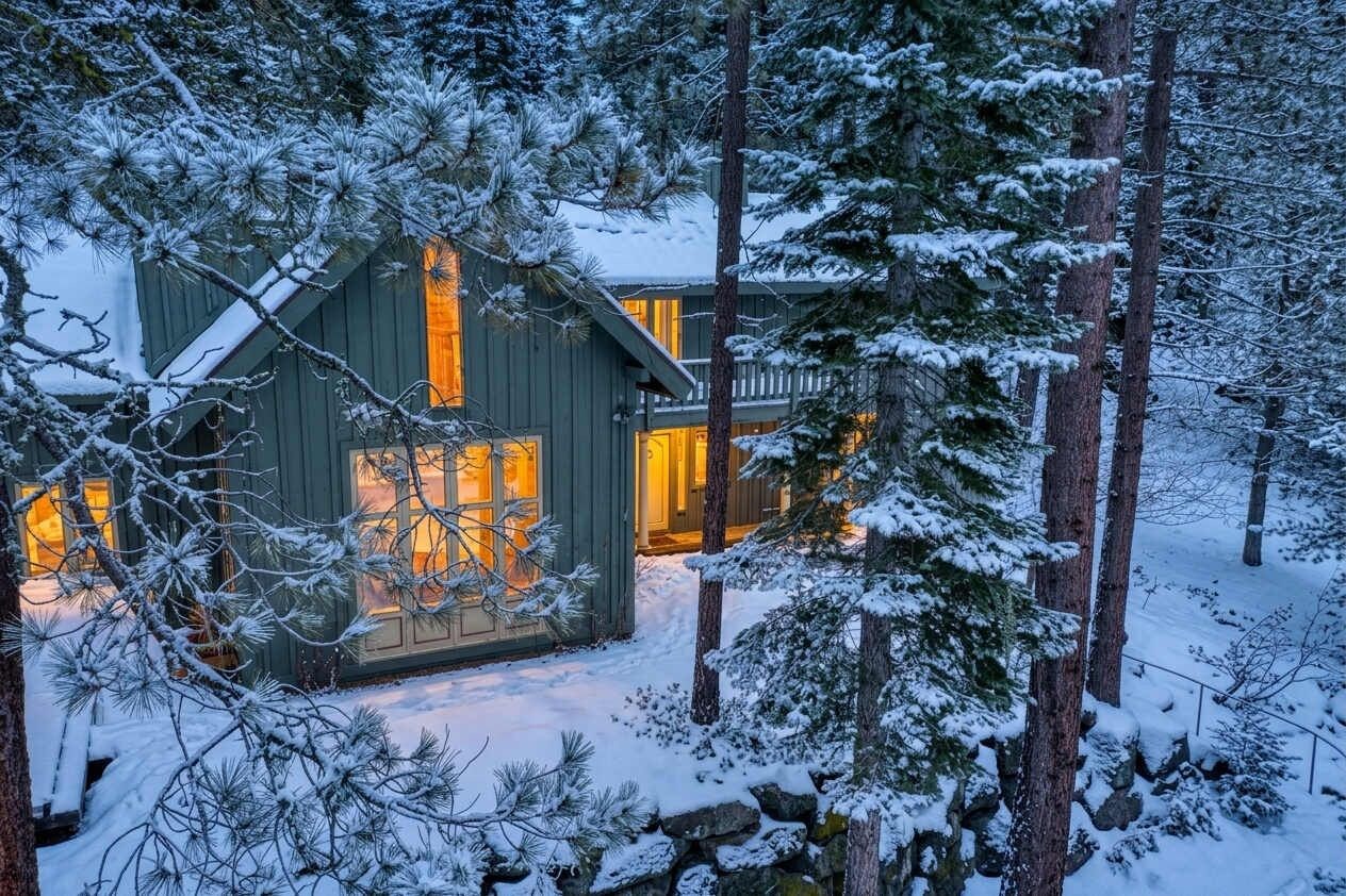 A cabin with a large window and a door, surrounded by snow-covered trees.