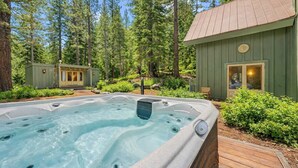A hot tub surrounded by a wooden deck, with a cabin and a small building in a forested area. - Olympic Valley Escape - Riverside Views + Hot Tub (Tahoe City)