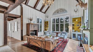 A spacious room with wooden floors, a large sofa, a dining table, and a chandelier. - Olympic Valley Escape - Riverside Views + Hot Tub (Tahoe City)