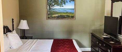 Ein Hotelzimmer mit Bett, Fernseher, Kommode, Lampe und einem Landschaftsbild.