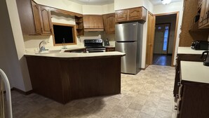 A kitchen with wooden cabinets, a stainless steel refrigerator, a stove, and a large island. - Studio 6 Lake George, NY - Adirondacks (Lake George)