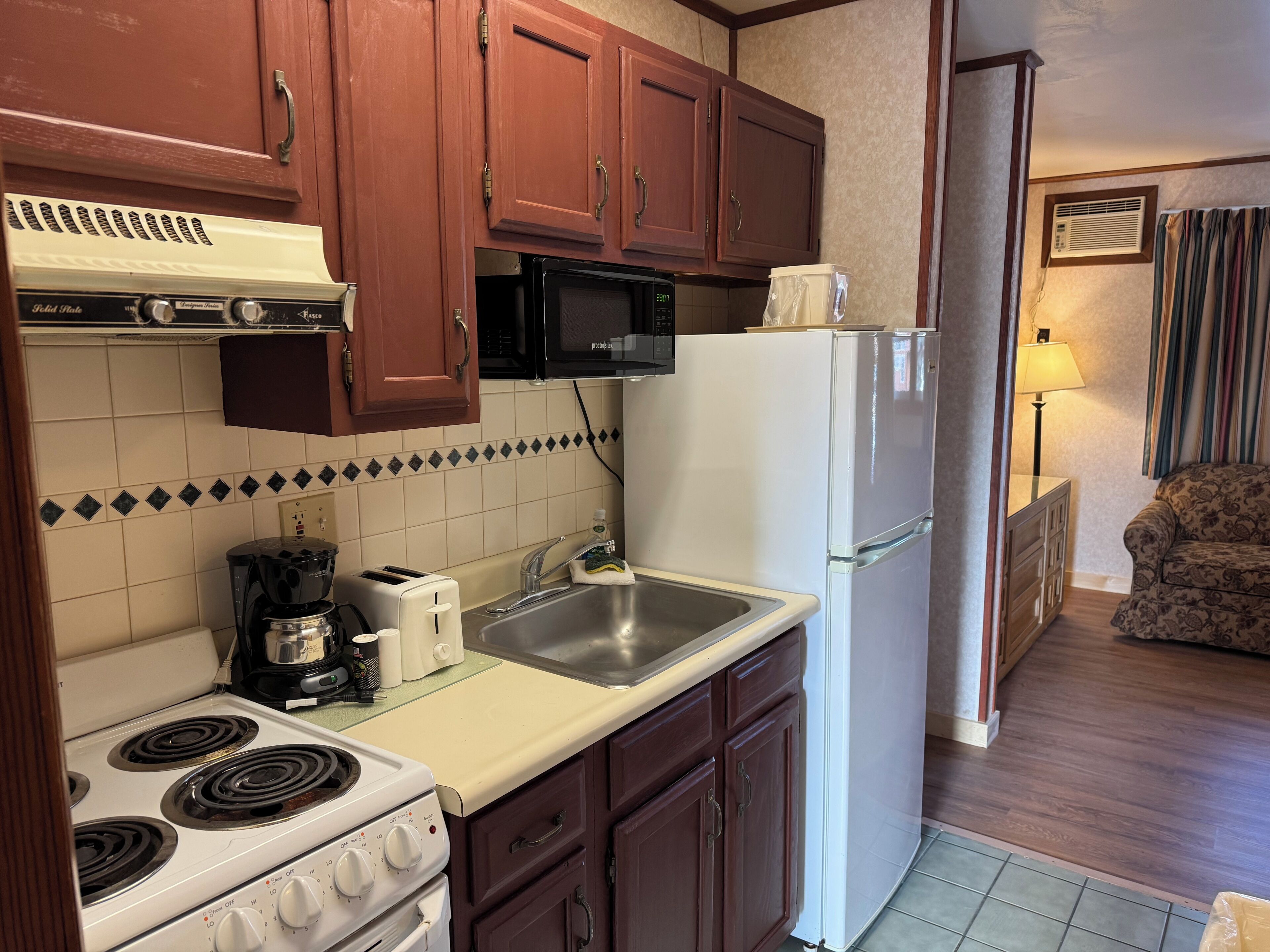 Una cocina con armarios de madera, microondas, refrigerador, estufa y lavaplatos.