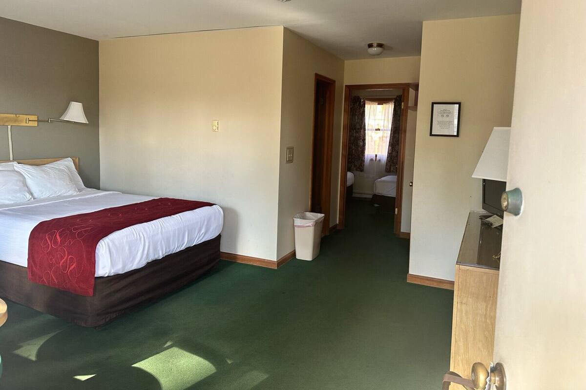 A hotel room with a large bed, a desk, and a chair. There is a door leading to another room.