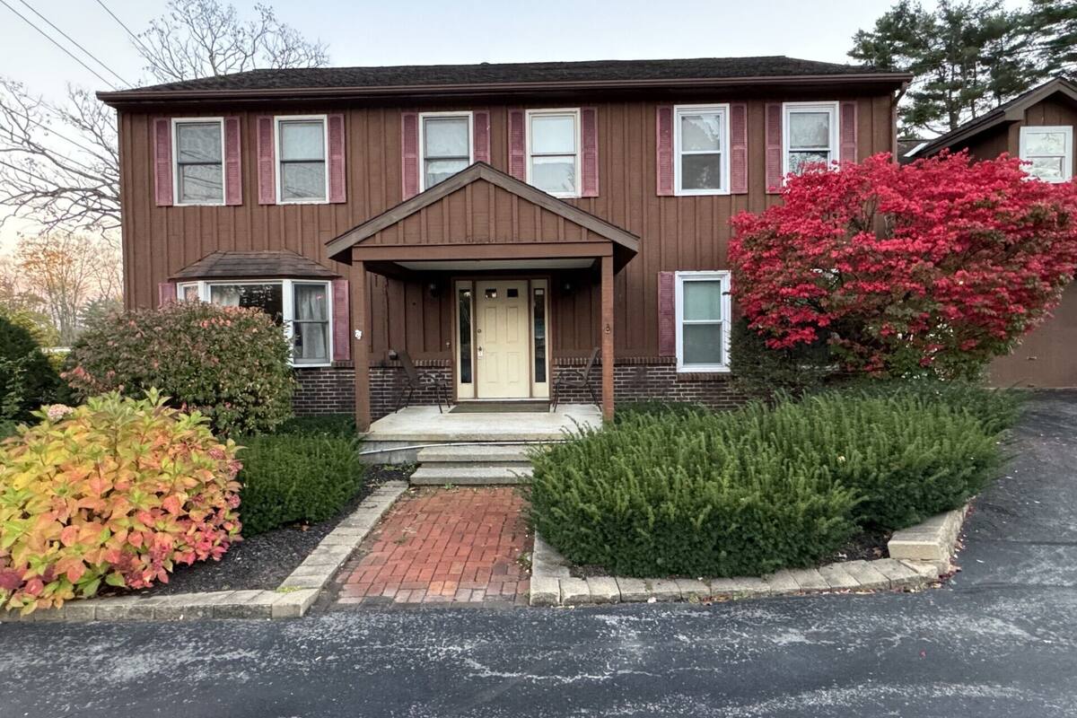 A two-story building with a central entrance, a brick pathway leading to the door, and a small porch area.