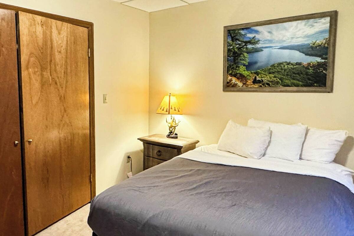 A bedroom with a bed, a nightstand, a lamp, a painting, and a wardrobe.