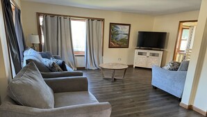 A living room with two sofas, a coffee table, a TV, and a painting on the wall. - Studio 6 Lake George, NY - Adirondacks (Lake George)