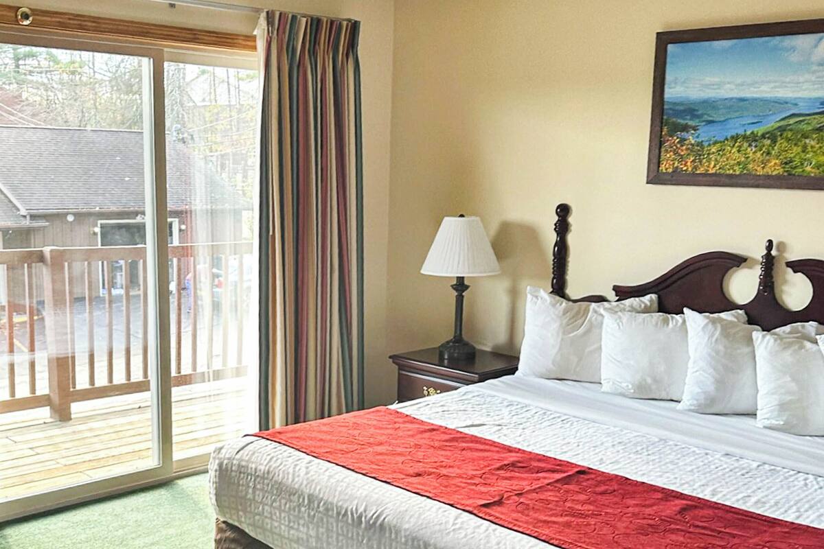 A hotel room with a bed, a nightstand, a lamp, a painting, and a sliding glass door to a balcony.