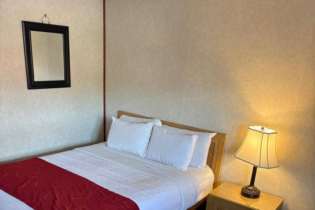 A neatly made bed with white linens and a red blanket, a bedside lamp, and a small wooden nightstand.