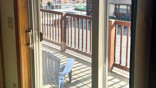 A view through a glass door of a balcony with a wooden railing, a blue chair, and a tiled floor. - Studio 6 Lake George, NY - Adirondacks (Lake George)