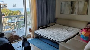 Een hotelkamer met een bed, een plafondventilator, uitzicht op zee en een balkon met buitenmeubilair.