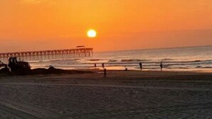 Een zonsondergang boven een strand met een pier die het water in reikt.