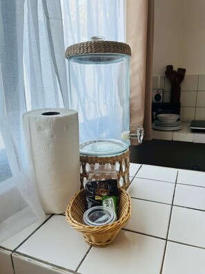 Eine Küchenzeile mit Wasserspender, Küchenpapierrolle und einem Korbwägelchen mit einer Dose und einer Packung.