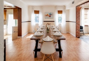 A dining room with a long wooden table set for a meal, white chairs, and a vase with flowers.