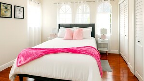 Un dormitorio con cama, mesitas de noche, una ventana y una puerta.