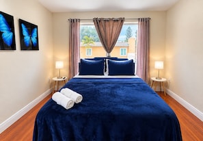 A hotel room with a large bed, two bedside lamps, a window with curtains, and two wall-mounted butterfly art pieces.