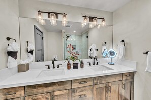Un baño moderno con un espejo grande, dos lavamanos, armarios de madera y luces decorativas.