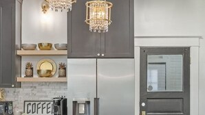 A modern kitchen with dark cabinetry, a stainless steel refrigerator, and two crystal chandeliers.