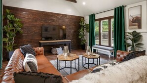 Een gezellige woonkamer met een leren bank, een salontafel en een televisie tegen een houten wand.