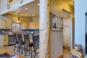 A rustic kitchen with wooden cabinets, a bar area with leather chairs, and a welcome sign. - Snow Worries (South Fork)