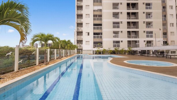 Una piscina con solárium alicatado, rodeada por una valla y palmeras.