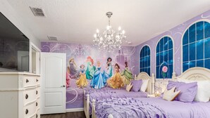 Ein Schlafzimmer mit einem großen Bett, einer Kristallleuchtre und Wandmalerei mit Prinzessinnen.