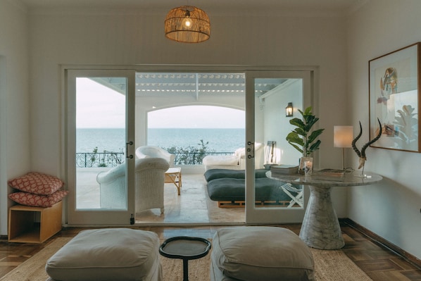 Une pièce avec vue sur la mer, un canapé blanc, une petite table ronde et une plante en pot.