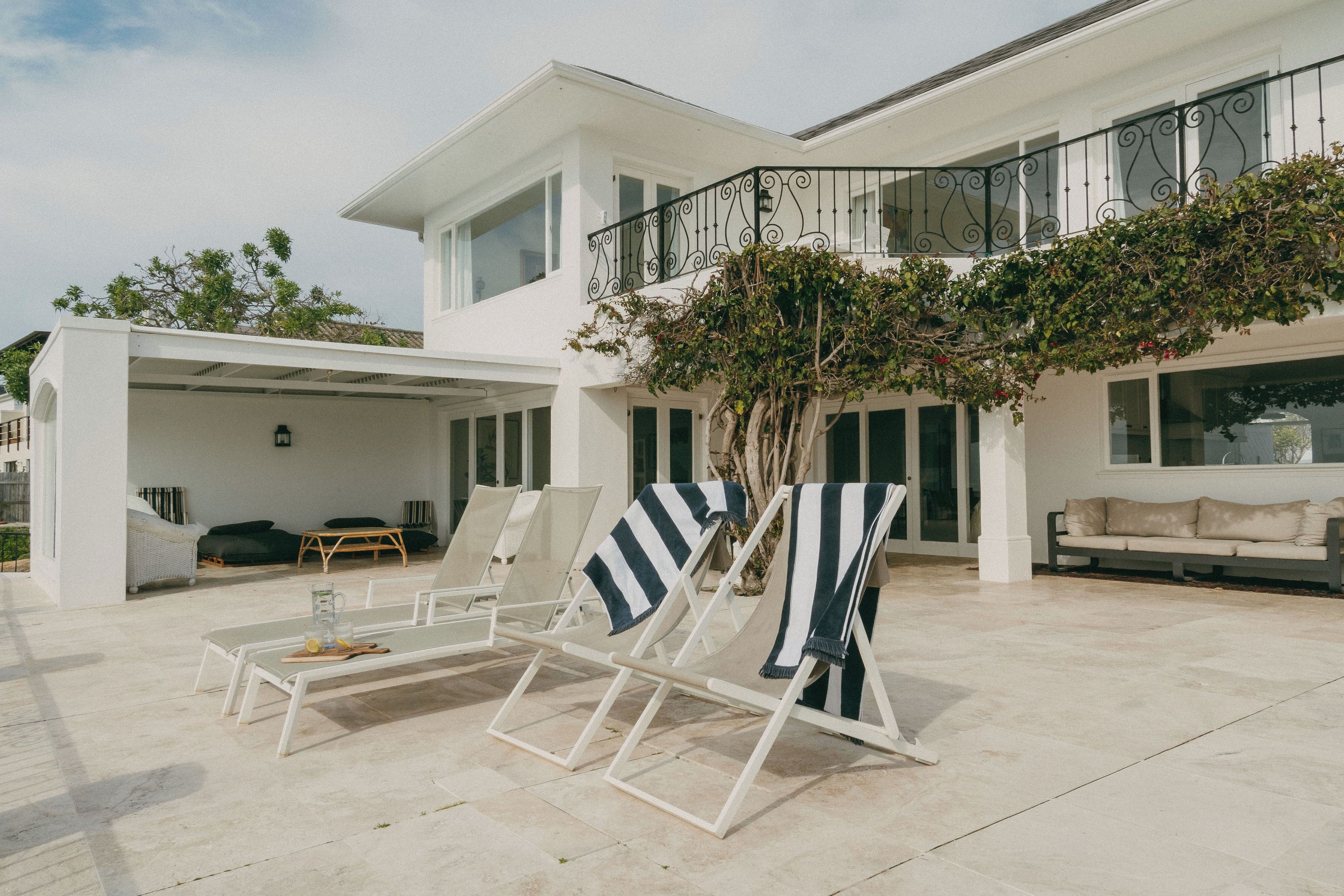A modern house with a covered patio, lounge chairs, and a dining area.