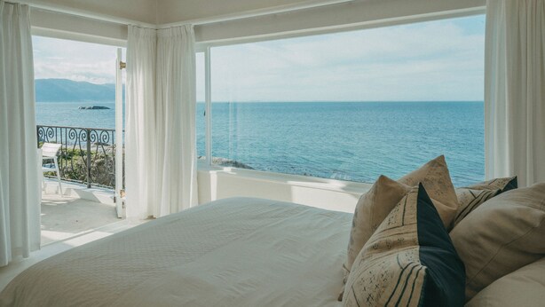 A bedroom with a large bed, white curtains, and a view of the sea through a balcony. - Links Crescent | Contemporary Coastal Sanctuary (Cape Town)