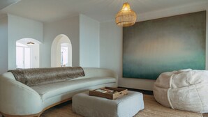 A modern living room with a sofa, ottoman, and bean bag, a large abstract painting, and a hanging light fixture. - Links Crescent | Contemporary Coastal Sanctuary (Cape Town)
