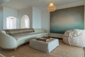 Una sala moderna con sofá, reposapiés y un sillón de peluche, un cuadro abstracto grande en la pared y una lámpara colgante.